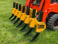 Thumbnail for A red John Deere tractor with a red rake attachment parked in a field of tall green grass. The sky is blue and there are a few white clouds in the distance.