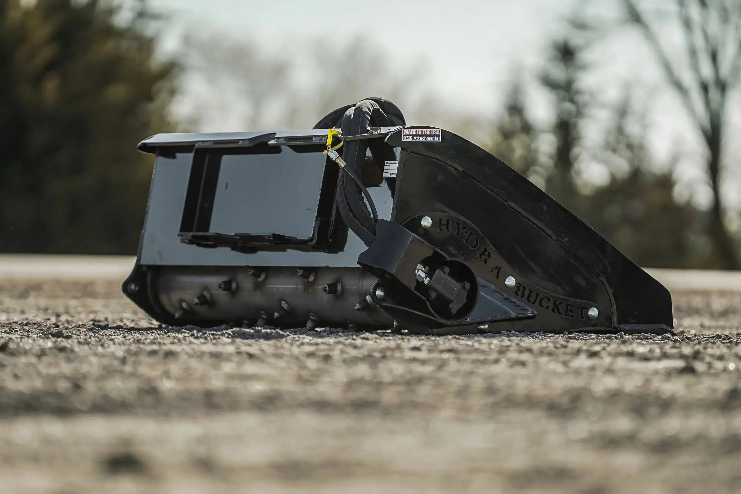 Hydra Bucket sitting on a gravel lot showing the backside of the bucket to display the power rake.