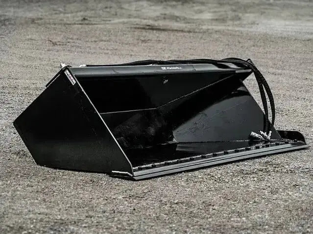 The image shows a black bucket sitting on top of a dirt road. The bucket is upright and empty. The dirt road is winding and dusty, and there are a few trees in the distance. The image is well-lit and in focus.