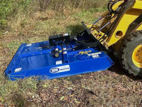 Thumbnail for The image shows a yellow skid steer with a blue mower attachment in a field. The tractor is parked on a dirt path, and the mower is raised off the ground. 