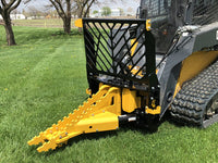 Thumbnail for Dominator tree puller: This yellow and black attachment is mounted on a skid steer, which is parked in a grassy field with trees in the background.