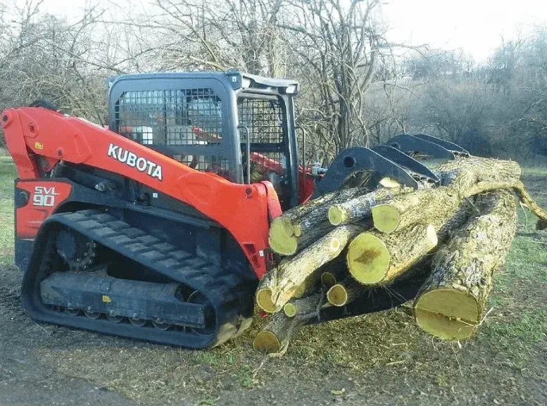 The skid-steer loader is equipped with a grapple attachment, which is a hydraulically operated claw-like device used for grabbing and lifting logs, branches, and other materials. In the image, the grapple is lowered and positioned near the front of the loader.