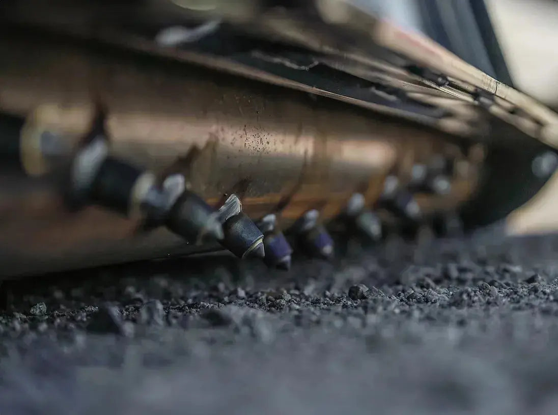 A detailed view of a metallic pipe, equipped with pointed protrusions, situated on asphalt.