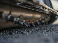 Thumbnail for A detailed view of a metallic pipe, equipped with pointed protrusions, situated on asphalt.