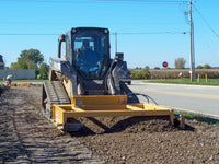 Thumbnail for A skid steer with a DoMor SSF-72 box grader attachment, parked on a gravel surface. The attachment is yellow with black branding and has an open-box design.
