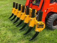 Thumbnail for A red John Deere tractor with a red rake attachment parked in a field of tall green grass. The sky is blue and there are a few white clouds in the distance. 