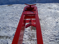 Thumbnail for A TM Manufacturing Pro 30 skid steer log splitter attachment in the snow. The splitter is bright red and has a black metal frame with red hydraulic hoses and a control panel